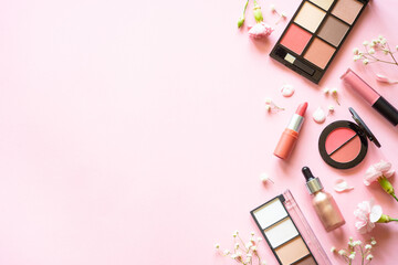Makeup professional cosmetics on pink background with flowers. Flat lay with copy space.