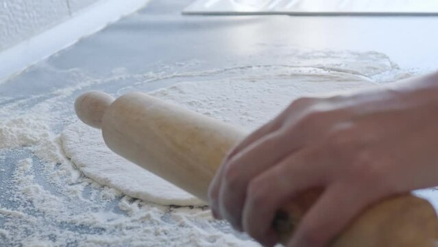 Cook rolls out the dough for pizza with a rolling pin. The cook rolls out the dough, chef is baking, bakery products, making the dough