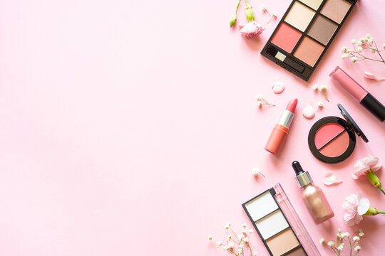 Makeup professional cosmetics on pink background with flowers. Flat lay with copy space.