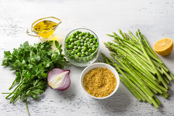 Ingredients for middle eastern tabbouleh salad. Bulgur, fresh young green asparagus, green peas, red onion, herbs, lemon and olive oil on a light blue background. Healthy vegan food.