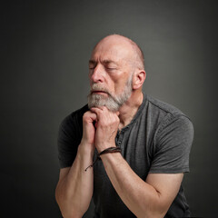 Head and shoulders portrait of bald and bearded senior man with closed eyes contemplating, meditating or praying