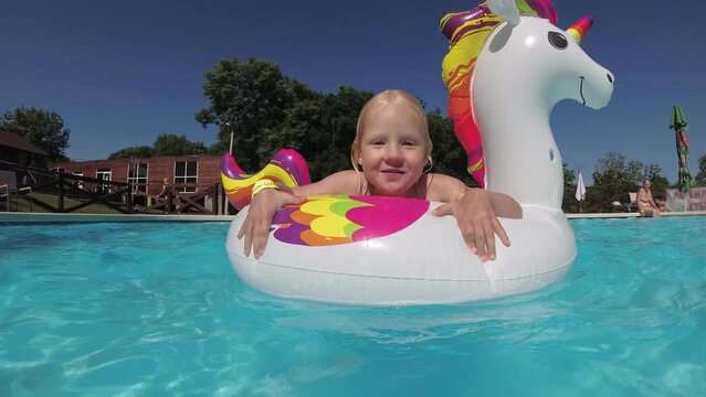 Happy child girl swims in a large inflatable circle in a summer outdoor pool