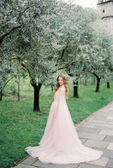 Bride in a pink dress with a cape stands near a green olive tree in a grove