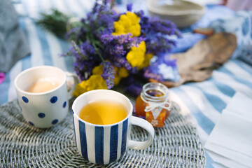 summer bouquet of yellow yarrow and violet lavender, 2 striped and polka dot cups of tea with milk and jar of tangerine jam on a striped picnic blanket with summer vibe - 520679400