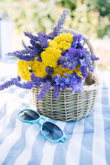 summer bouquet of yellow yarrow and violet lavender in a basket with bright eye glasses on a striped picnic blanket with summer vibe - 520679444