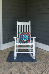 A stamped concrete front porch with a white rocking chair with a colorful pillow