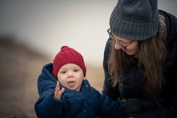 Niño bebé con gorro de lana rojo y campera sonriendo y mirando a la cámara y jugando con su...