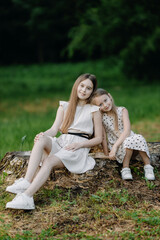 Two little girls in summer dresses sitting on a stump in a park and laughing