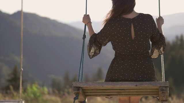 Young single woman feels free flying in a cliff rope wooden swing chair on top pf the mountain enjoying the breathtaking panorama