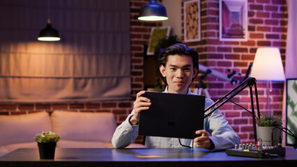 Asian man talking about laptop product and technology, doing review of wireless computer on podcast...