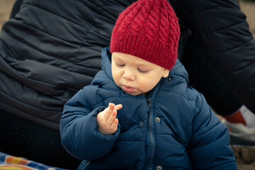 Niño bebé con gorro de lana rojo mirando sus manos con arena en la playa en otoño e invierno