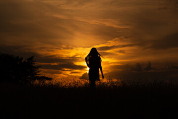 Silhouette of a woman in a dress standing in a meadow at sunset