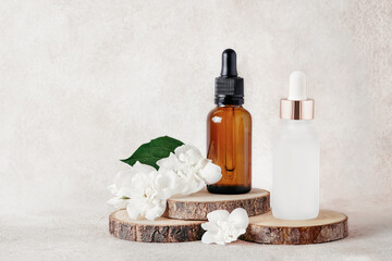 Fototapeta na wymiar Glass dropper bottles for medical and cosmetic use and jasmine flowers on wooden cut. SPA concept.