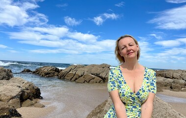 woman in a bright dress on the beach an adult woman with great pleasure sits on the sea on her face is written relaxation bliss and buzz. High quality photo