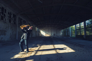 Man playing jazz on saxophone in the abandoned factory building on a sunny summer day