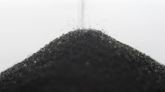 Grains of black sand and quartz are falling in a glass hourglass.