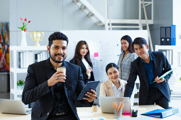 Young indian handsome bearded coworkers with coffee cup at camera smiling feel happy. Background...