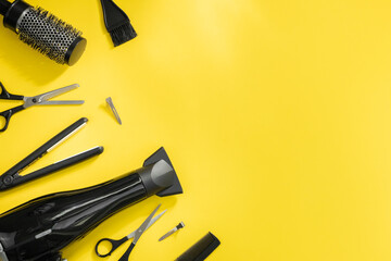Scissors, hair dryer, hair straightener, combs, brush and hair clips lie on a yellow background