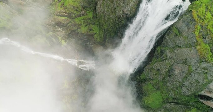 Dramatic Vøringsfossen waterfall rush splash down rocky foggy canyon; drone