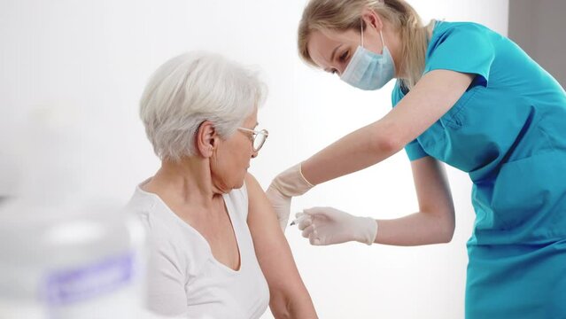An elderly worried woman getting vaccinated for virus protection by a professional nurse at the hospital. High quality 4k footage