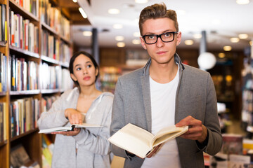 attractive young students studying in library, reading and discussing books