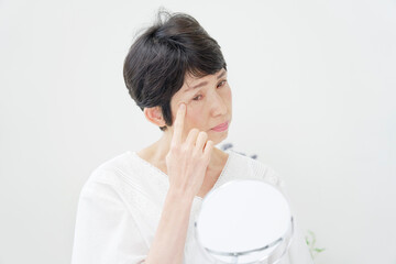 リビングで鏡で顔を見て悩むシニア女性