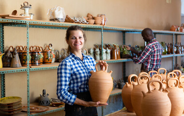 Woman and man artisans in apron having ceramics in store warehouse. High quality photo