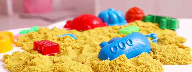 Bright kinetic sand and toys on white table indoors. Banner design