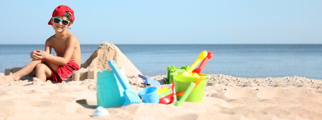 Cute little child and plastic toys at sandy beach on sunny day. Banner design