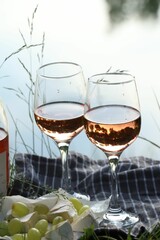 Delicious rose wine, cheese and grapes on picnic blanket near lake