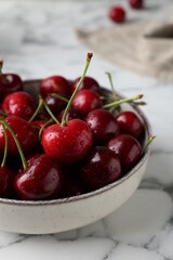 Fresh ripe cherries with water drops in bowl on white marble table, closeup