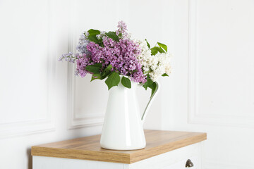 Beautiful lilac flowers in vase on wooden table near white wall