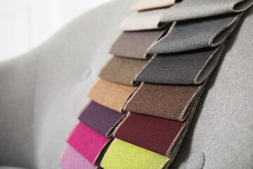 Catalog of colorful fabric samples on grey sofa, closeup. Space for text