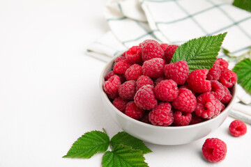 Bowl of fresh ripe raspberries with green leaves on white table. Space for text