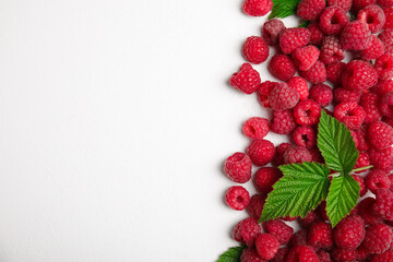 Fototapeta premium Fresh ripe raspberries with green leaves on white background, flat lay. Space for text