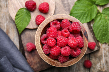Bowl with fresh ripe raspberries and green leaves on wooden table, flat lay
