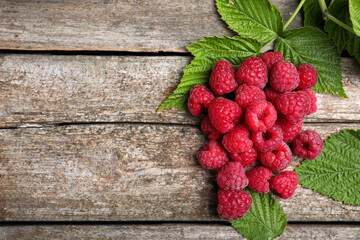 Fresh ripe raspberries with green leaves on wooden table, flat lay. Space for text