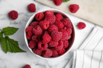 Bowl with fresh ripe raspberries on white marble table, flat lay