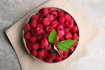 Bowl of fresh ripe raspberries with green leaves on grey table, top view