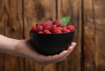 Woman holding bowl with fresh ripe raspberries against wooden background, closeup - obrazy, fototapety, plakaty