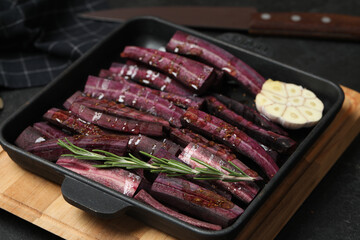 Black raw cut carrot with garlic and rosemary in baking dish on black table, closeup