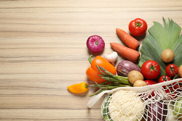 Fresh vegetables in eco mesh bag on wooden table, flat lay. Space for text