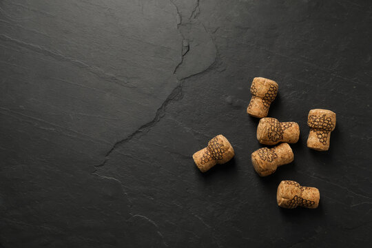 Sparkling wine corks with grape images on black table, flat lay. Space for text