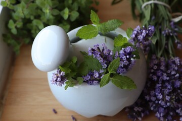 Mortar with fresh lavender flowers, mint and pestle on wooden table, closeup