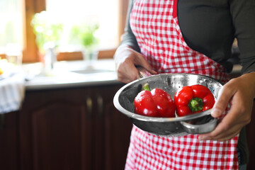 Woman holding colander with fresh bell peppers in kitchen, closeup. Space for text