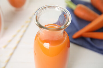 Freshly made carrot juice in glass bottle on white table, closeup