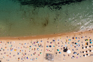 Birds eye view of crouded beach. People lying on sand and swimming in water.