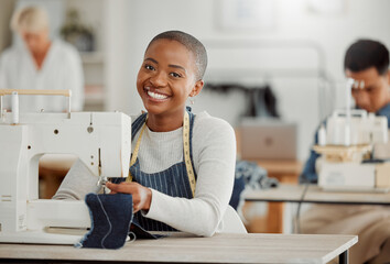 Happy, creative black fashion student or designer sitting and smiling in class by a sewing machine...