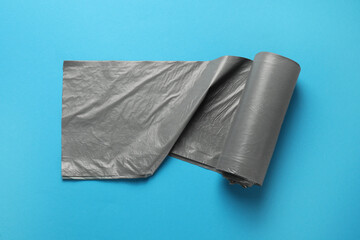 Roll of grey garbage bags on light blue background, top view. Cleaning supplies