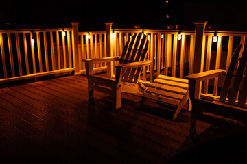 white Adirondack chairs on rooftop deck with white fence and string lights at night